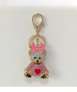 Détail d'un porte-clés ours avec nœud rose et cœur rouge serti de cristaux blancs et roses