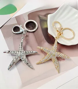 Détail de porte-clés étoile de mer dorés et argentés sertis de strass sur un coquillage blanc