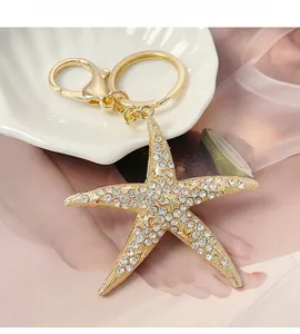 Gros plan sur porte-clés étoile de mer dorée avec strass blancs sur plateau coquillage