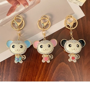 Dettaglio di tre portachiavi a forma di scimmia con strass in blu, rosa e nero su legno