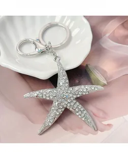 Gros plan d'un porte-clés étoile de mer en métal argenté et strass brillants sur coquillage