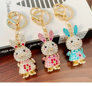Three rhinestone rabbit keychains in pink, white, and blue colors on a wooden background