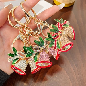 Handheld Christmas bell keychain with red and pink rhinestones on a wooden background