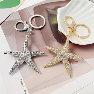Porte-clés étoile de mer étincelant avec strass en or et argent sur un plateau de coquillage
