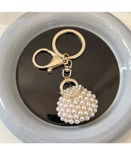 Detailed view of elegant gold pearl handbag keychain with crystal rhinestones on blue tray