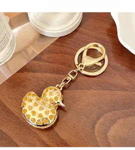 Close-up of golden duck keychain with hollow heart patterns on a wooden surface
