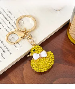Close-up of yellow rhinestone duck keychain with a white bow on a wooden desk background