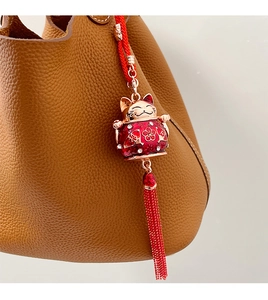 Macro detail of red Maneki-Neko charm with gold floral design on a leather handbag
