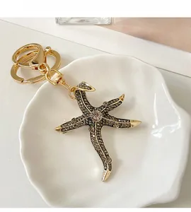 Detailed close-up of a golden starfish keychain with gray rhinestones on a white shell plate