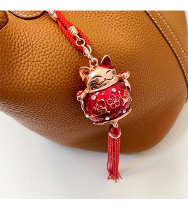 Detailed close-up of a lucky cat charm with a red tassel on a brown leather handbag