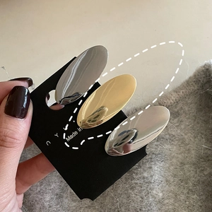 Close-up of three oval metal hair clips in gold and silver on a display card