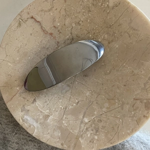 Minimalist silver mirror metal duckbill hair clip with sleek oval shape on marble tray