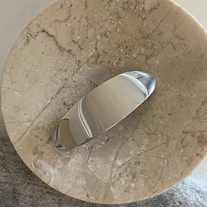 Minimalist silver metal hair clip with polished mirror finish on marble surface