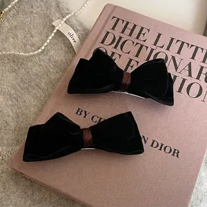Vintage black velvet bow hair clips with brown thread accent on a soft pink background