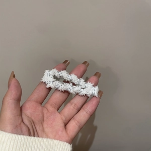 Detail of a white tweed hair clip with silver metallic threads and plush texture on a hand