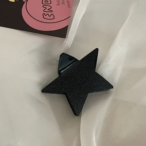 Dettaglio di una pinza per capelli a stella Y2K in acetato con finitura opaca glitterata