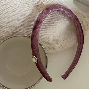 Detail of purple velvet headband with pearl accent on a beige ceramic bowl background