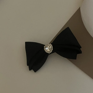 Détail d'une barrette nœud en satin noir avec un grand cristal en forme de cœur