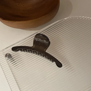 Gros plan d'une pince à cheveux translucide marron foncé sur un plateau en verre chic