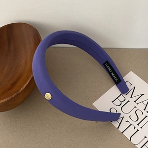 Détail du serre-tête en satin violet avec étiquette faite main et ornement doré