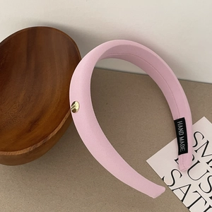 Gros plan sur le serre-tête en satin rose avec emblème doré et étiquette Hand Made