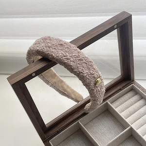 Close-up of pink tweed sponge headband with gold metallic logo on a wooden box