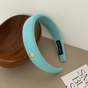 Détail d'un serre-tête en satin vert menthe avec emblème doré et étiquette faite main