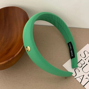 Détail du serre-tête en satin vert avec emblème doré et étiquette faite à la main
