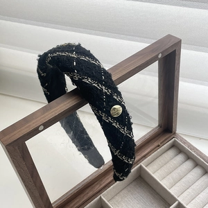 Close-up of black tweed headband with gold thread and metallic buckle on wooden case