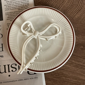 Detailed view of a creamy white bow-shaped metal hair claw clip on a tray with newspapers