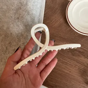 Close-up of a large cream-colored metallic hair claw clip held in hand for size detail