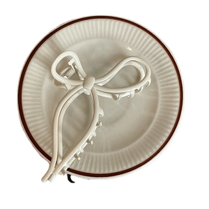 Elegant cream white bow-shaped metal hair claw clip displayed on a ceramic plate