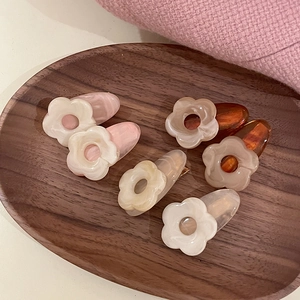 Floral acetate hair clips in pink marble, beige, and amber colors on a wooden tray