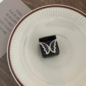 Elegant black square hair claw clip with rhinestone butterfly detail on ceramic tray