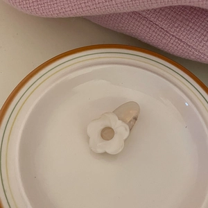 Detailed view of a minimalist white flower acetate hair clip on a white ceramic plate