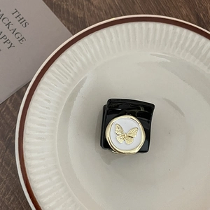 Detail of a mini black hair claw clip featuring a gold butterfly emblem on white enamel