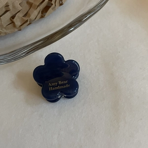 Mini pince à cheveux fleur bleu foncé en acétate avec inscription dorée Amy Bear sur blanc