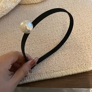 Minimalist black elastic pearl headband with a large white pearl on a cozy beige background