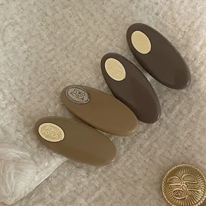 Set of four latte-colored oval hair clips with gold metal plates on knit background