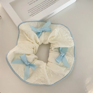 Elegant cream ruffled scrunchie with light blue satin bows in a minimalist aesthetic
