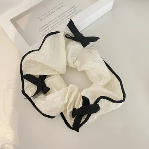 Elegant white scrunchie with black trim and bows for a stylish minimalist hairstyle