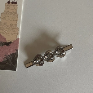 Clip para el pelo plateado con tres corazones de cristal en fondo de color