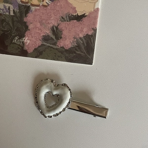Primer plano de un clip de pelo de corazón plateado con esmalte blanco y bordes ondulados