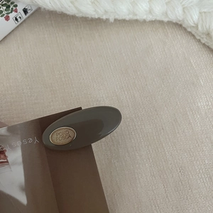 Latte-colored oval hair clip with gold metal accent on beige textured fabric