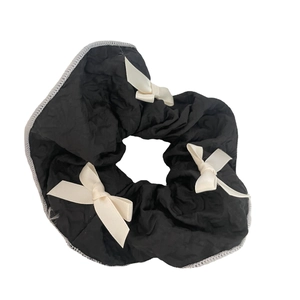 Elegant black scrunchie with pleated fabric texture and three creamy ribbon bows