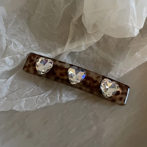 Detail view of acetate leopard print hair clip featuring three sparkling heart crystals