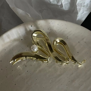 Pince à cheveux dorée ondulée avec perle blanche sur un plateau en céramique