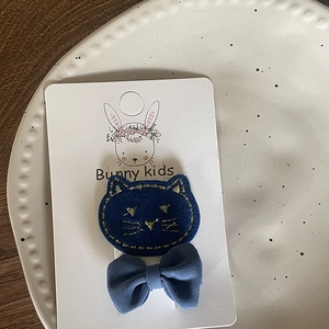 Detail view of blue cat-shaped hair clip and fabric bow on Bunny Kids display card