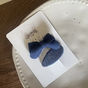 Detail view of navy blue fabric bow and woven oval hair clips for girls on a display card