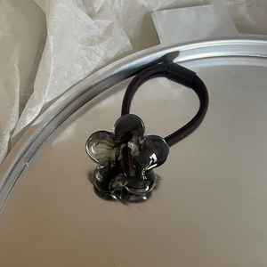 Detail of a translucent grey flower hair tie on a metallic tray with elegant texture